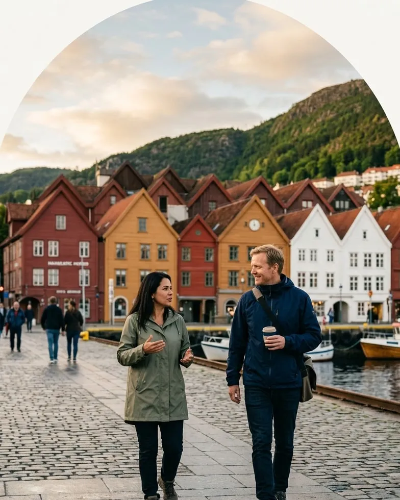 Duas pessoas conversando no cais de Bergen, com as casas de madeira coloridas de Bryggen ao fundo.